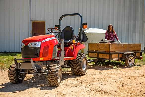 Massey Ferguson GC1700 Series sub-compact tractor parked in front of barn with utility trailer in background