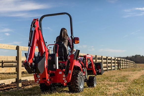 Thumbnail forRear view of Massey Ferguson GC1700 Series sub-compact tractor with backhoe and woman operator driving along fence line