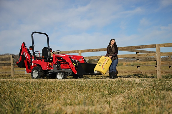 Massey Ferguson GC1700 Series sub-compact tractor with front loader and backhoe next to woman carrying livestock feed