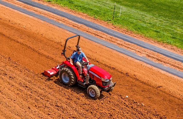 Massey Ferguson 1800 E Series compact tractor with rotary tiller working across garden rows