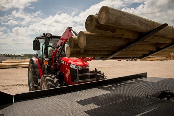 Massey Ferguson 4700 Series utility tractor loading wooden posts with front-end loader and pallet forks