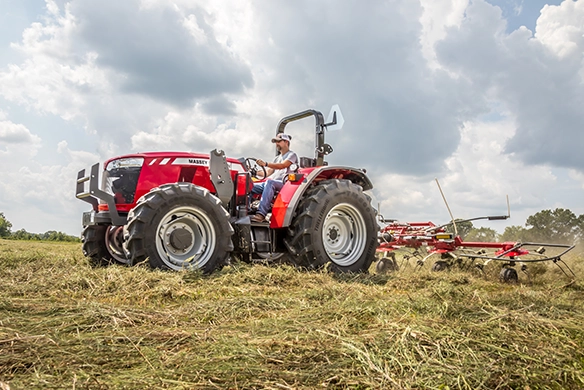 Massey Ferguson 4700 Series open platform utility tractor raking hay under partly cloudy skies