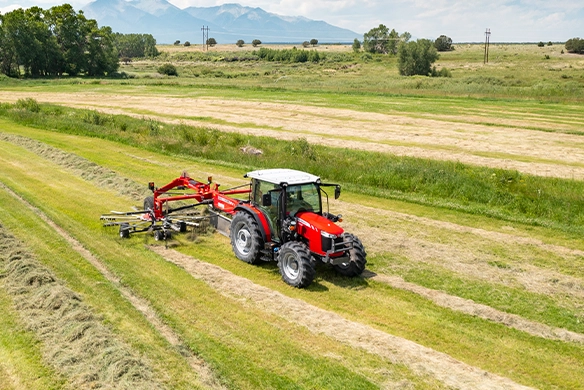 Massey Ferguson 4700 Series cab utility tractor raking hay with MF RK802 rotary rake