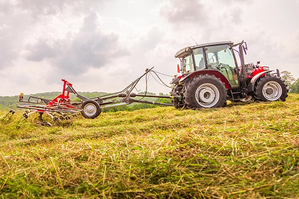 Massey Ferguson 4700 Series utility tractor pulling TD 775 TRC rotary tedder across a hayfield.