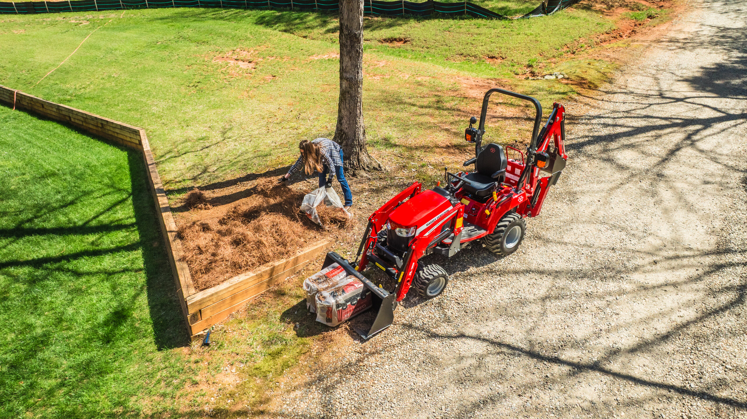 Massey Ferguson 1GC Series sub-compact tractor assisting with landscaping and mulch work near tree line