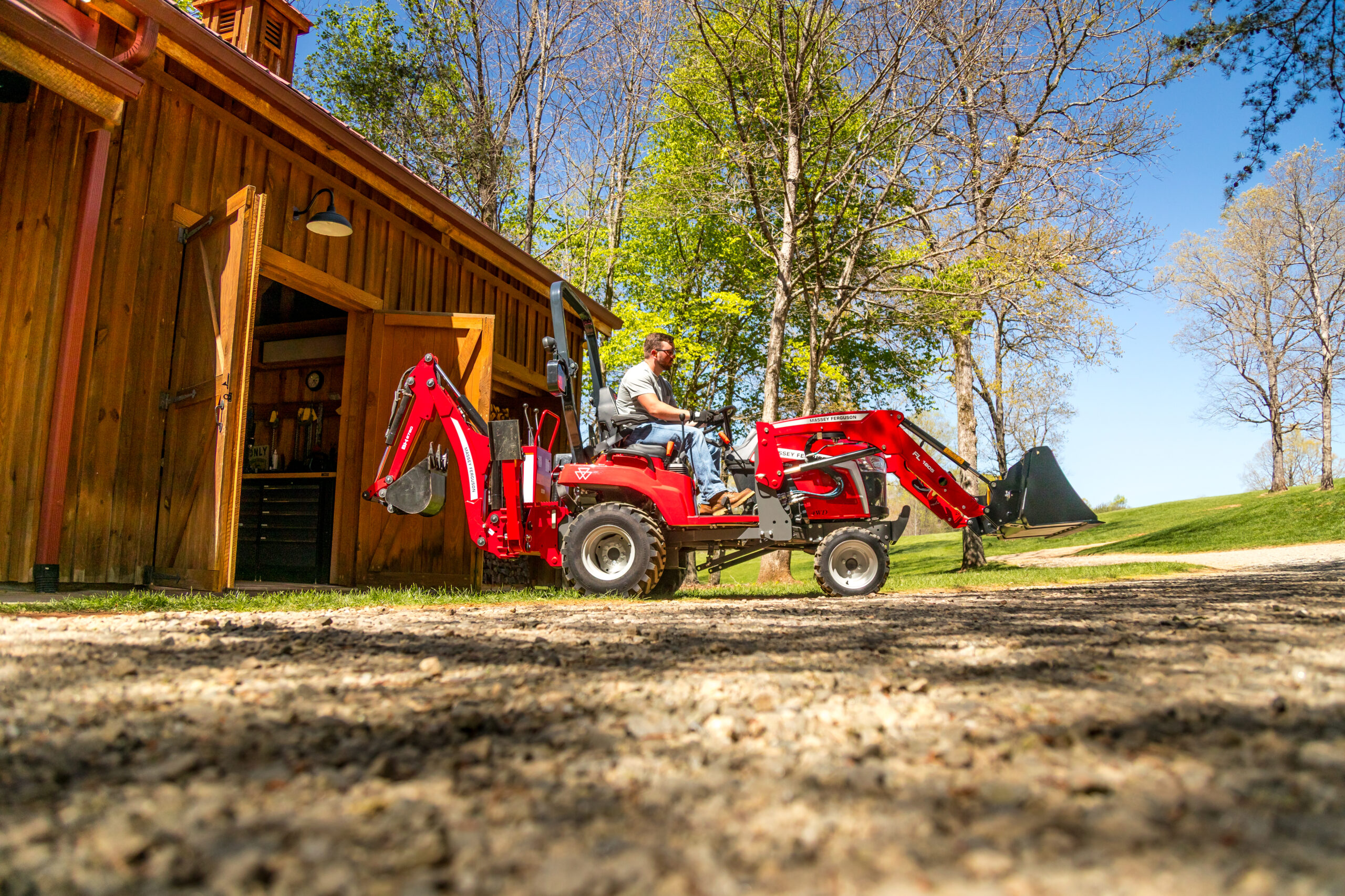 Massey Ferguson 1GC Series sub-compact tractor with loader and backhoe parked beside wooden barn