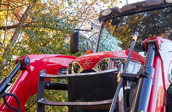 Close-up of the Massey Ferguson 1M Series compact tractor front grill and loader arms, set against autumn foliage.