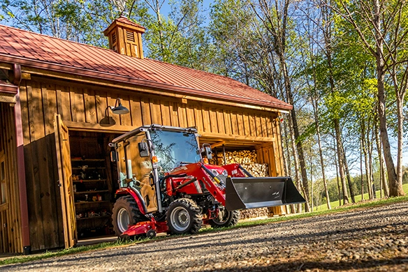 Massey Ferguson 1M Series compact tractor with front loader and mid mower deck, pulling out from a barn.