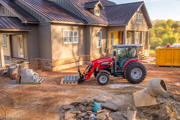 Massey Ferguson 2M Series compact tractor moving concrete cinder blocks at a residential construction site.