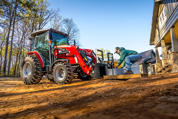 Man unloading cinder blocks from a pallet being carried by a Massey Ferguson 2M Series compact tractor.