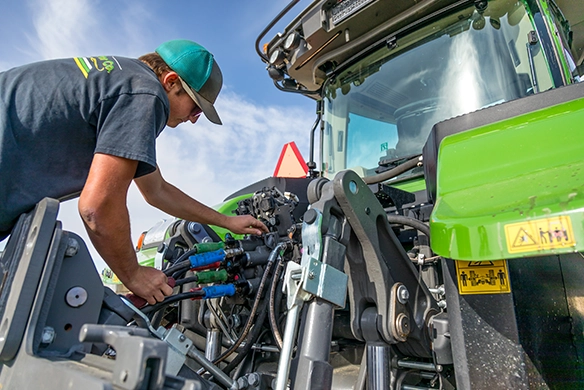 Quinn Ag service technician working on a Fendt tractor outside under a bright blue sky in Southern California.